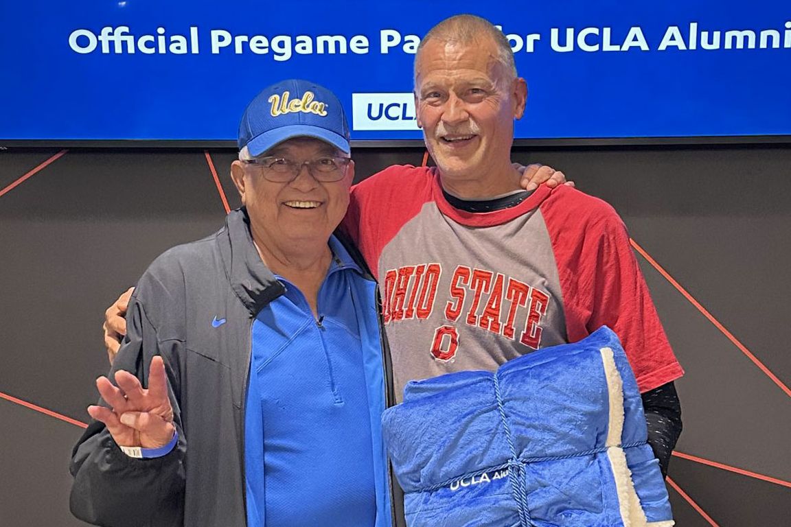 Man in UCLA hat and blue shirt with arm around man in red and gray Ohio State shirt