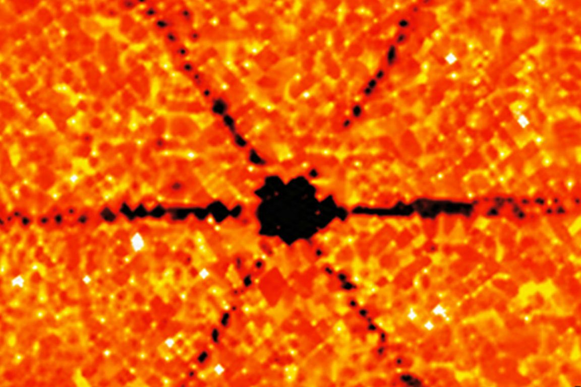 A dense black cluster sits at the center, with narrow dark ray-like streaks extending outward in multiple directions across a mottled orange-and-yellow background, illustrating directional heat flow through the material.