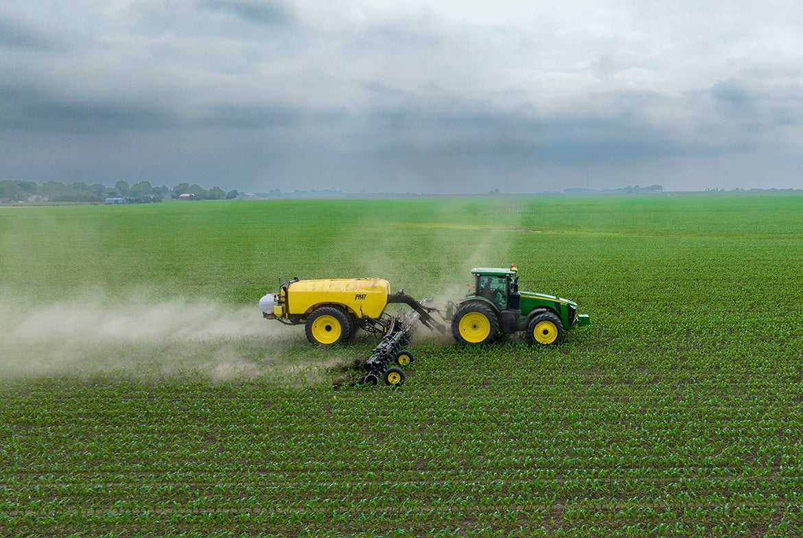 A green-and-yellow tractor spraying crops in a field